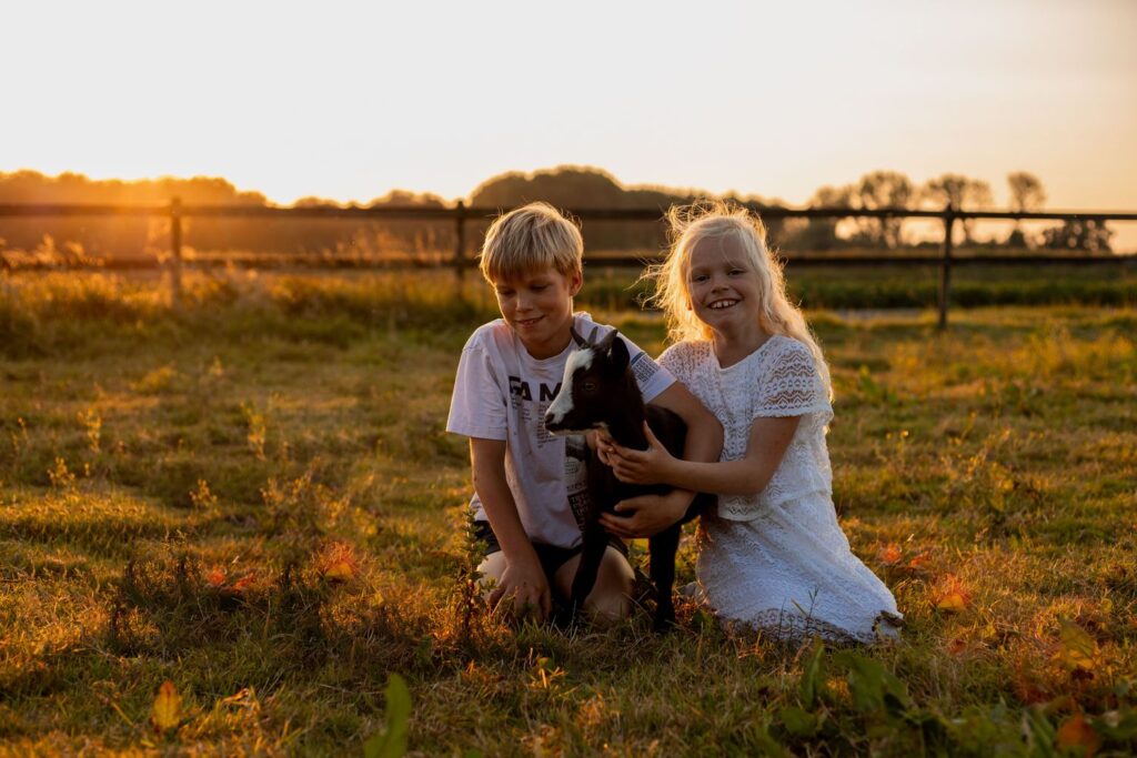 broer en zus op de foto met een geit bij zonsondergang