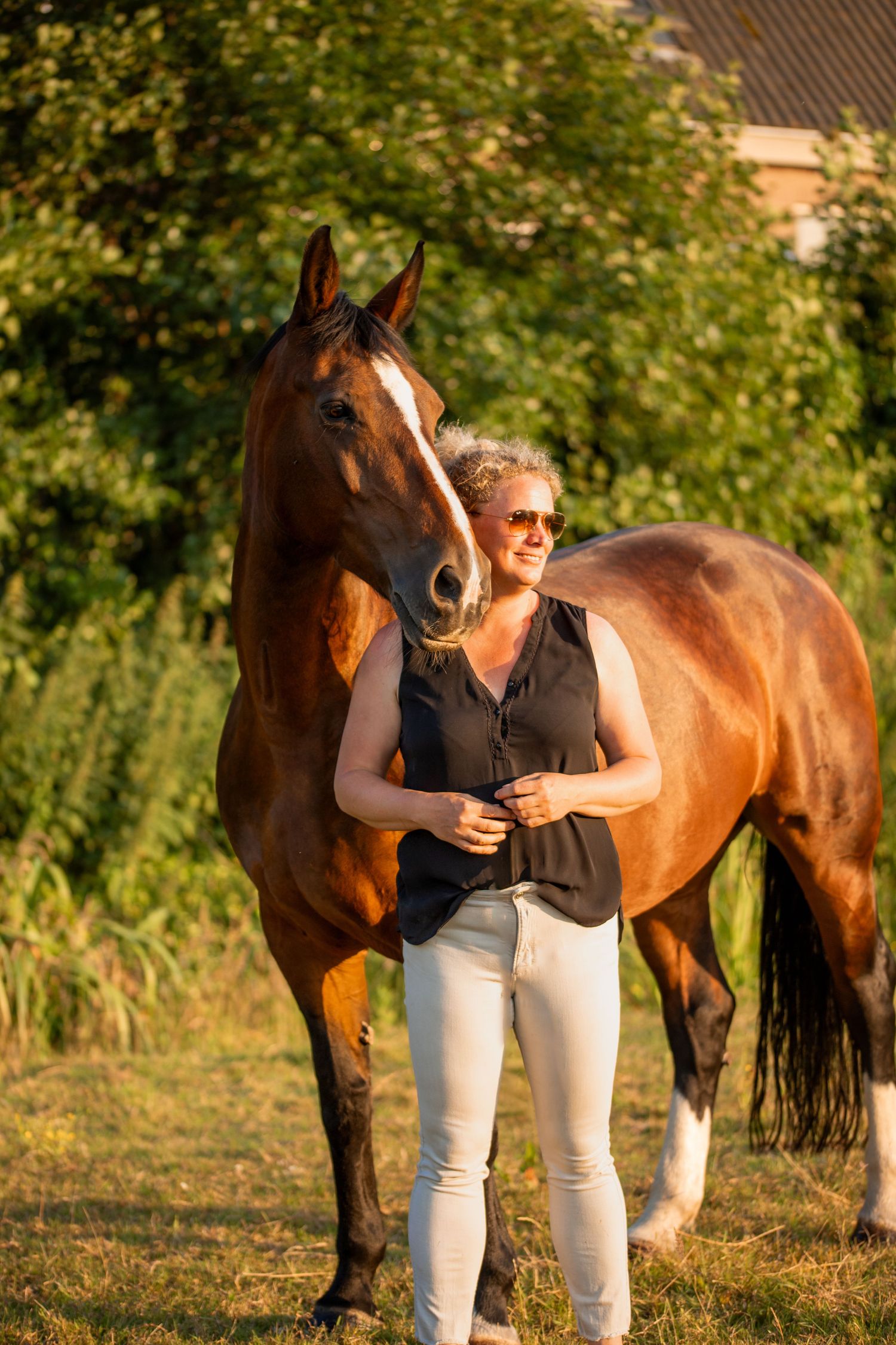 een blonde vrouw staat voor haar paard die kijken samen naar links paard kijkt over haar schouder