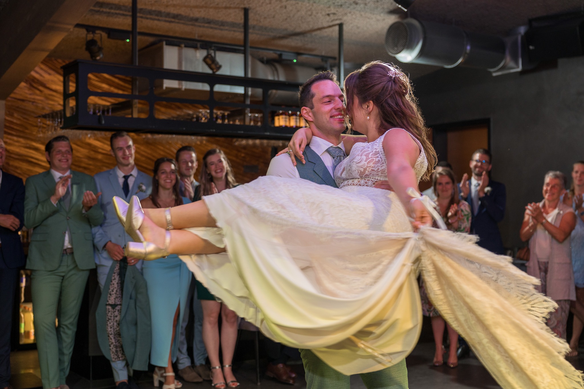 Bruidegom tilt zijn bruid op tijdens hun openingsdans Tijdens het feest tilt de bruidegom zijn bruid vol trots op, terwijl de gasten klappen en glimlachen – een stralende start van de dansvloer. trouwen bij Lakehouse Rotterdam.