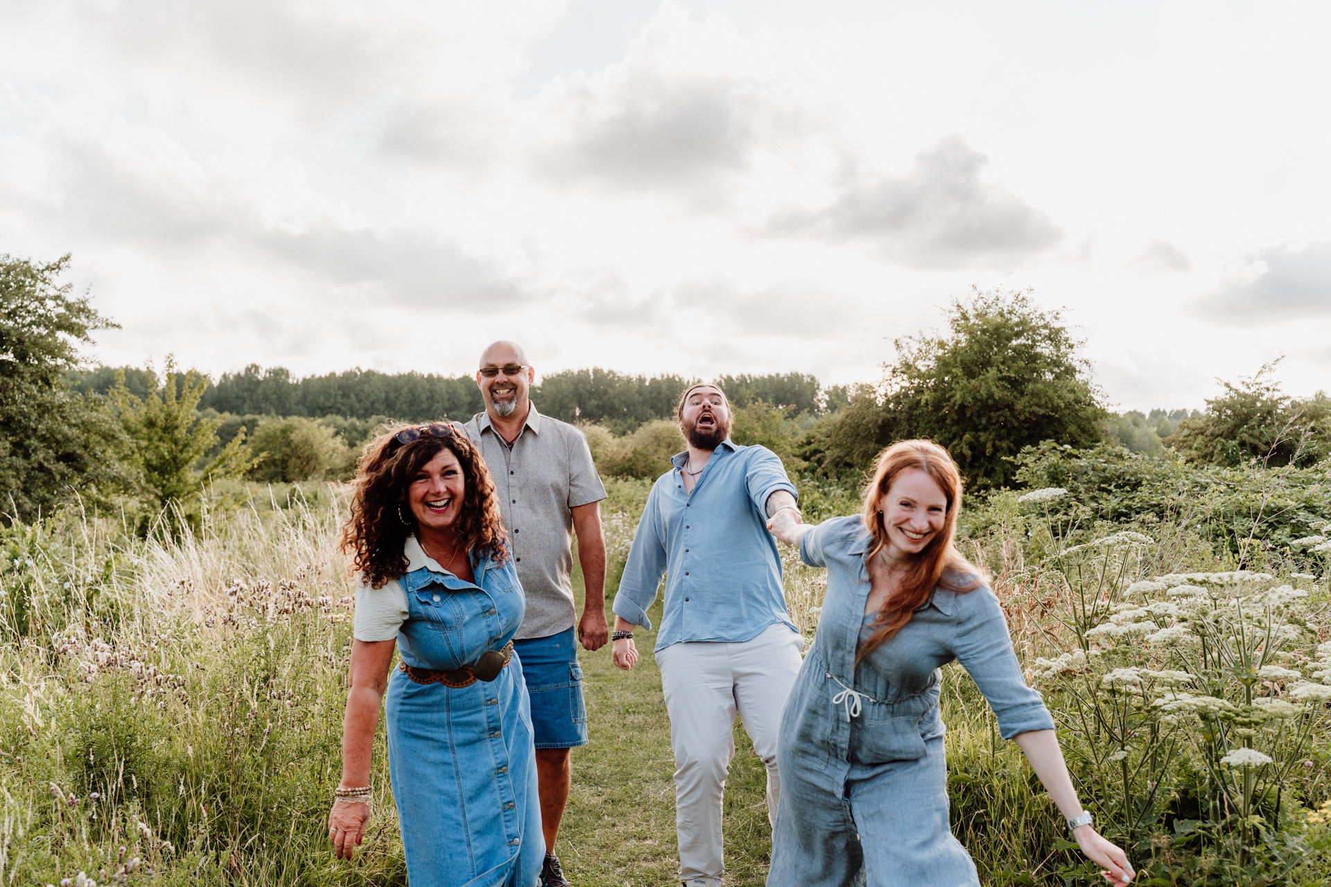 Vrolijk gezin dat hand in hand door het hoge gras wandelt tijdens hun familieshoot in de Broekpolder in Vlaardingen.