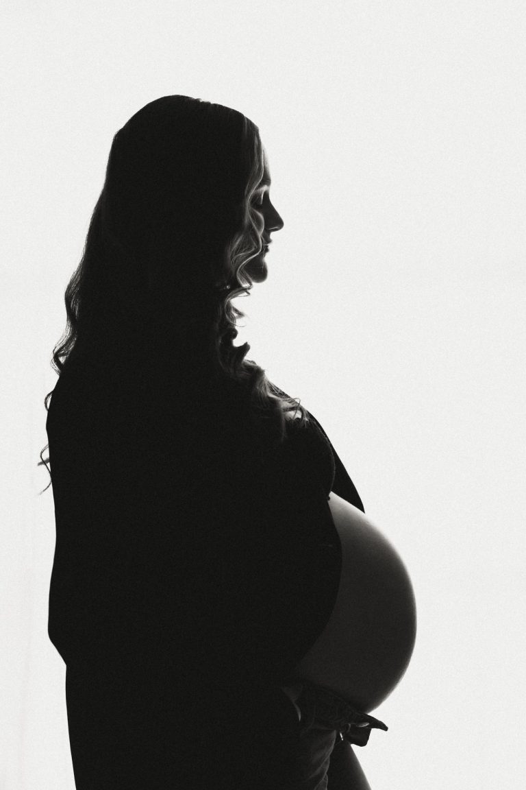 Zwart-wit silhouet van zwangere vrouw met ronde babybuik tegen licht doek, zwangerschapsshoot studio Zuidland