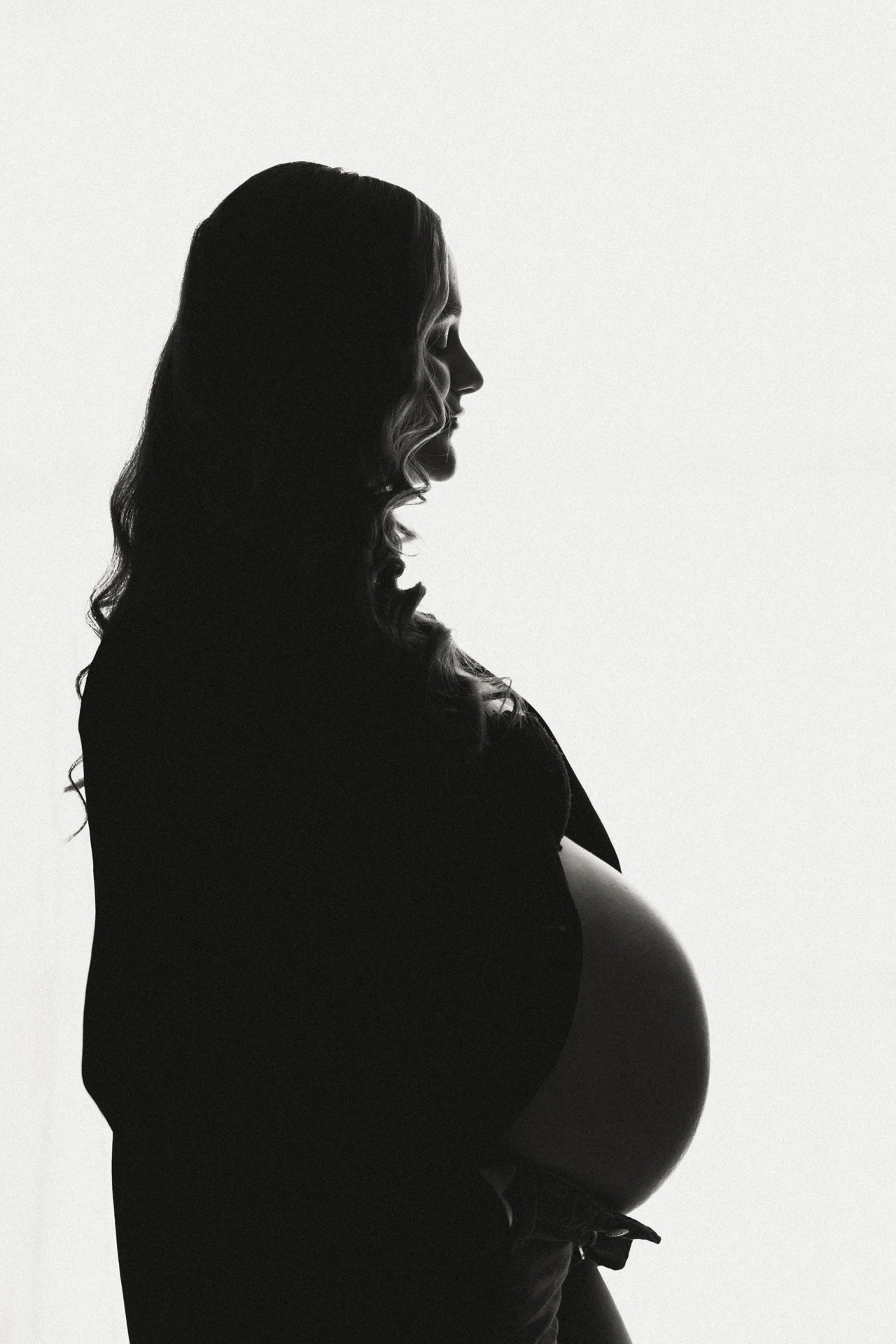 Zwart-wit silhouet van zwangere vrouw met ronde babybuik tegen licht doek, zwangerschapsshoot studio Zuidland